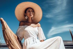 Beautiful spectacular young woman model in a white dress and hat against a bright blue sky on a sunny day. Generative AI Generative AI